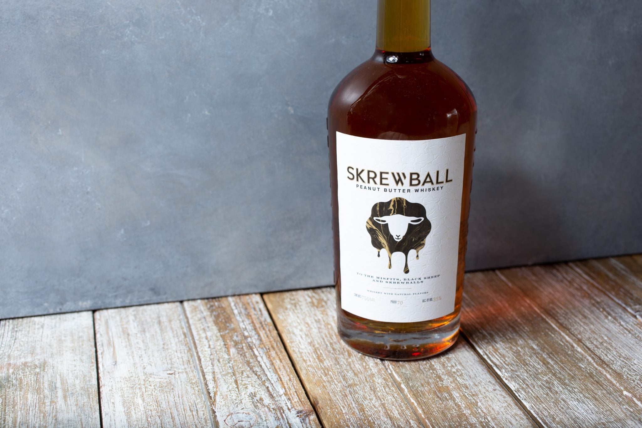 A Skrewball Peanut Butter Whiskey bottle on a wooden surface in front of a grey background