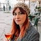 Woman with red hair and hat on drinking a cocktail outside a bar