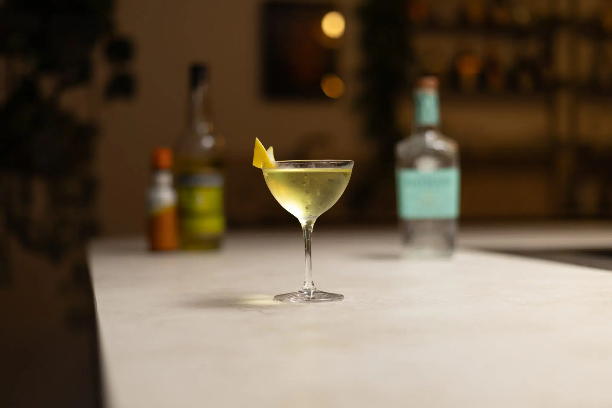 Old Tom Gin, yellow Chartreuse, and orange bitters laid out on a white bar table