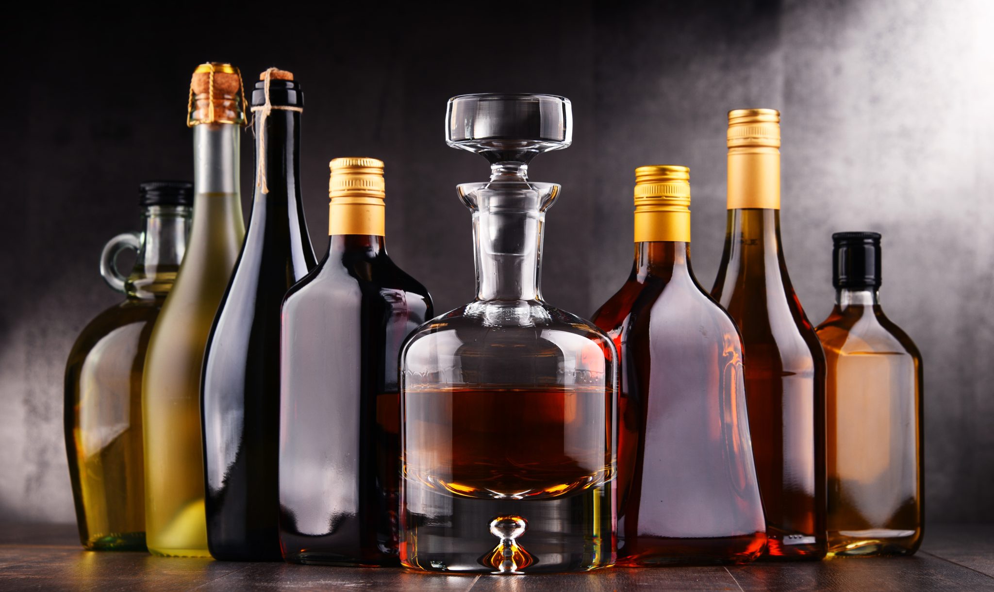 A shot of different types of containers for liquors and spirits, on a brown surface and in front of a dark grey background