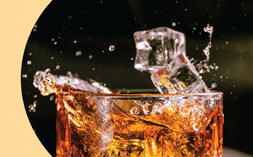 A close shot of ice cubes falling and splashing a drink in a rocks glass