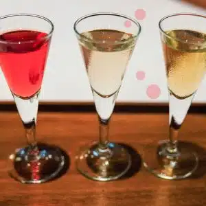 Three glasses with aquavit spirit, one red, one transparent and one yellow, placed over a dark brown wooden tray.