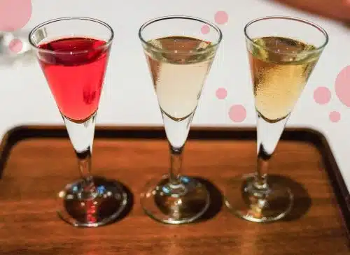 Three glasses with aquavit spirit, one red, one transparent and one yellow, placed over a dark brown wooden tray.