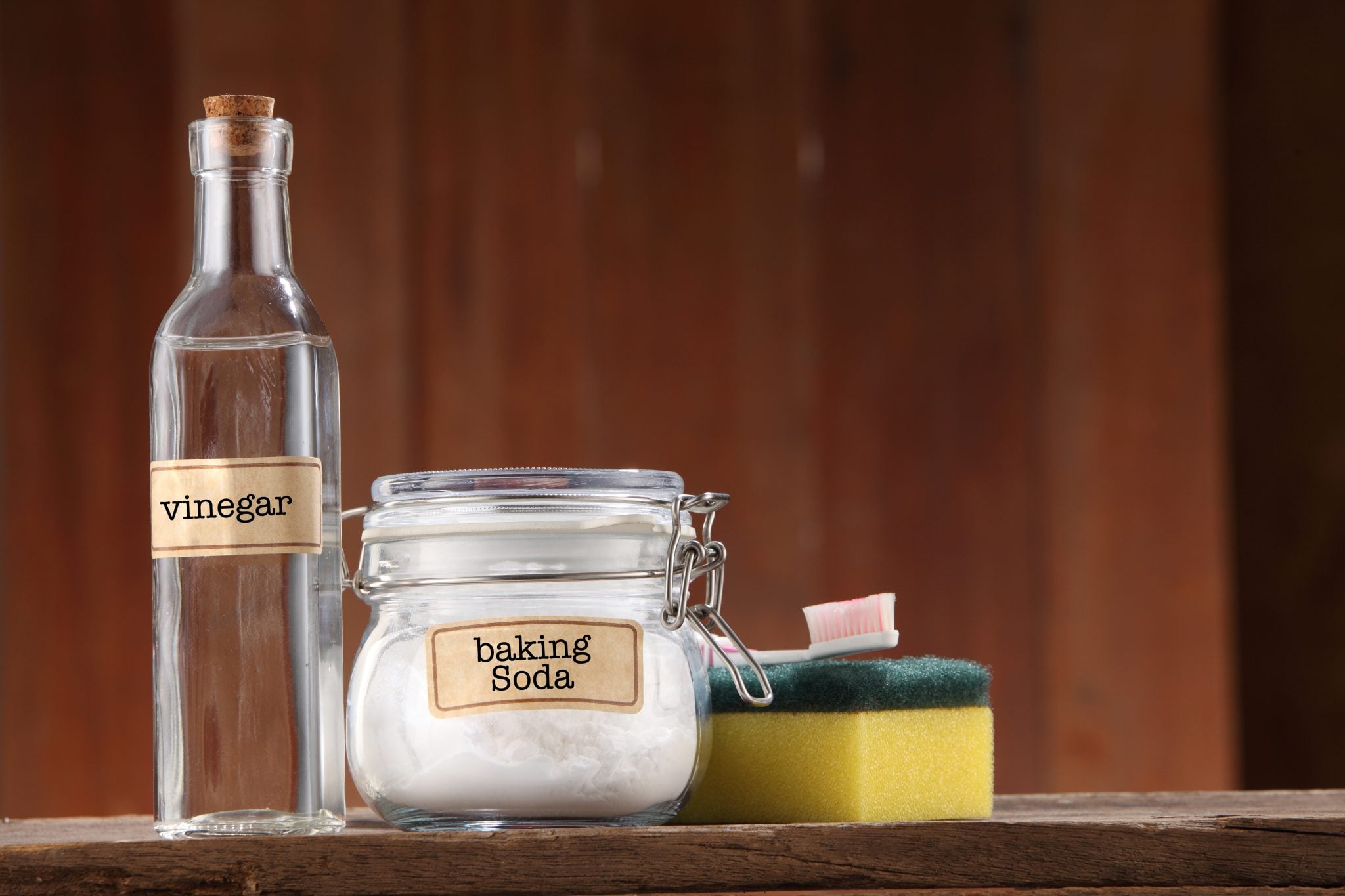 A shot of Baking Soda, Vinegar, a sponge and a toothbrush on a wooden background