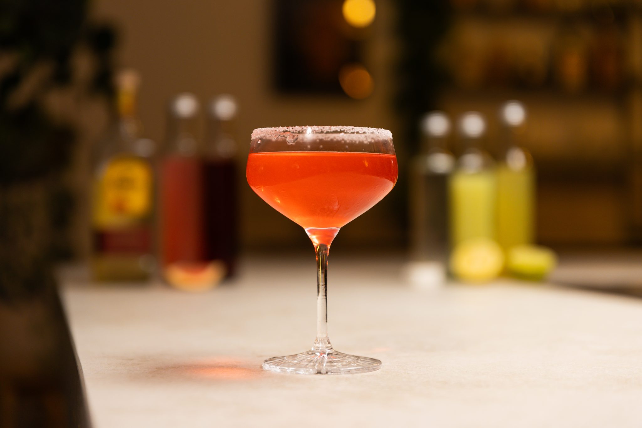 Tequila reposado, pink grapefruit juice, cranberry juice, simple syrup, sugar cubes, pink grapefruit, lime juice, lime, lemon juice, lemon, and salt laid out on a white bar table