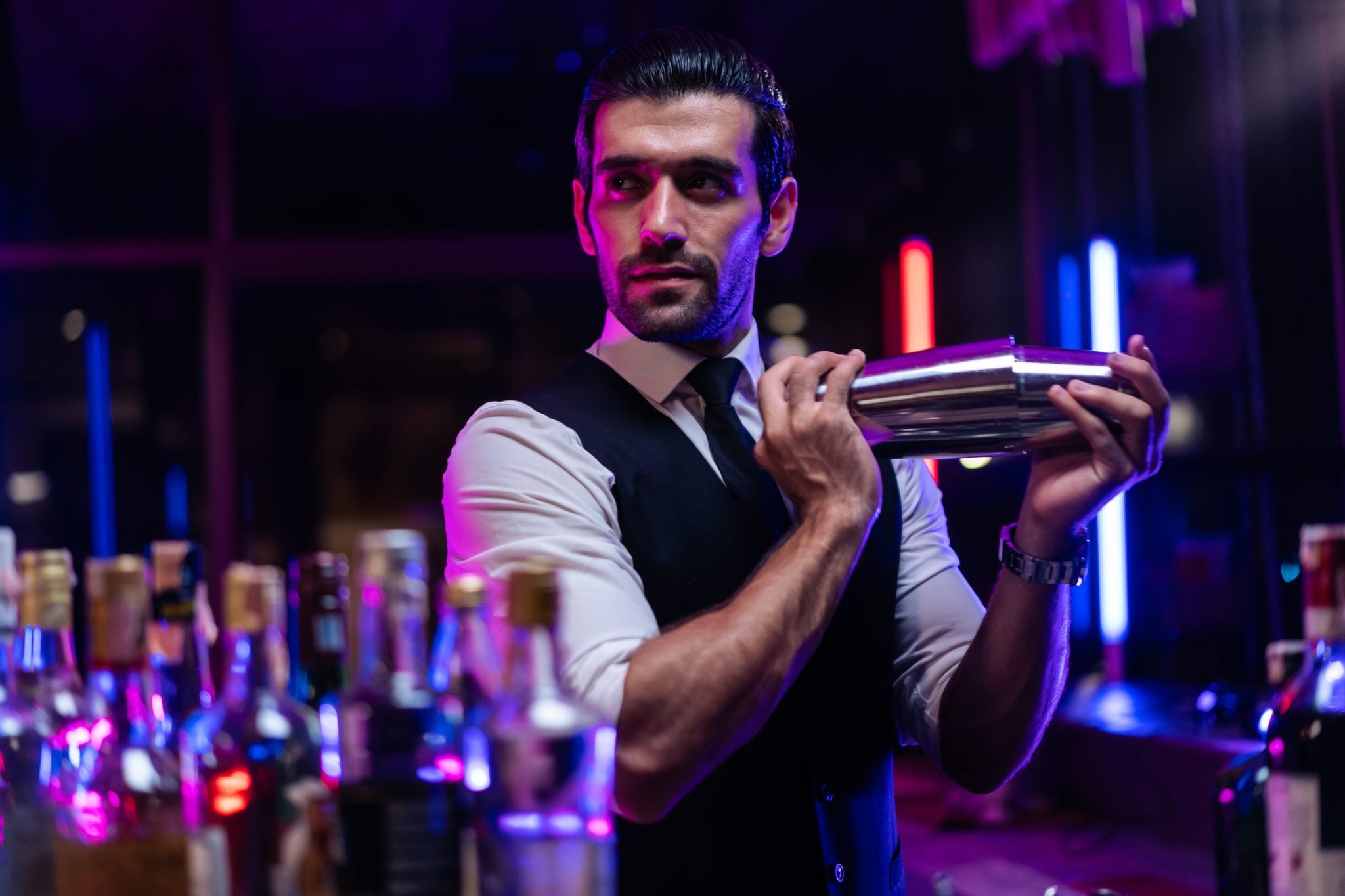 A shot of a bartender at night in a bar shaking a cocktail