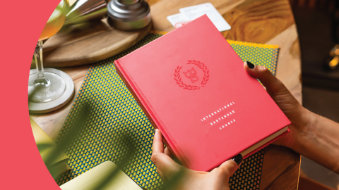 A shot of a person holding a book of the European Bartender School on top of a wooden table