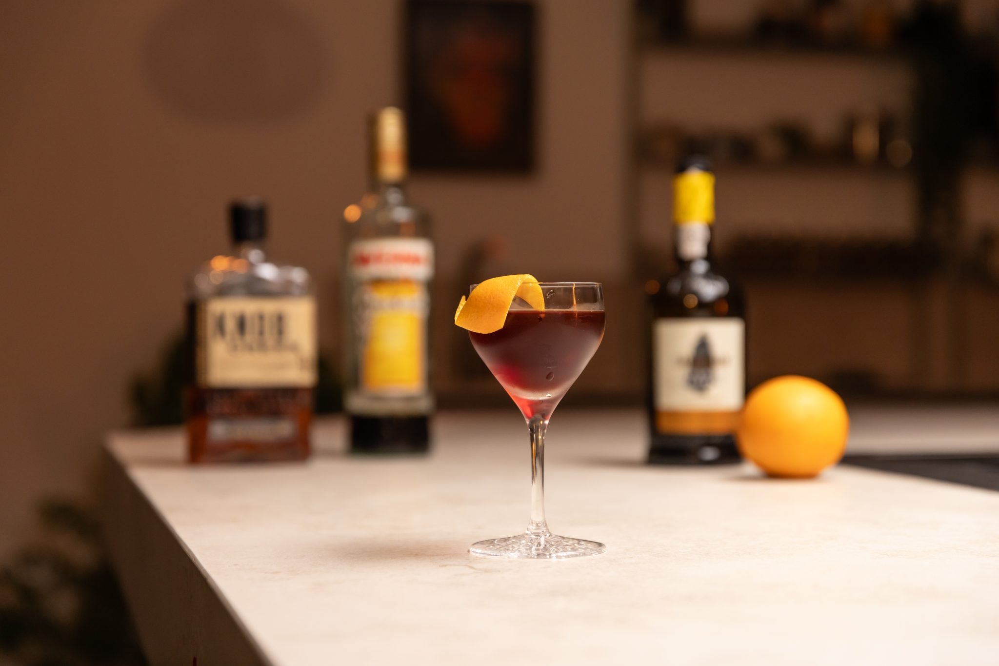 Averna Amaro, Tawny Port, Bourbon and an orange laid out on a white bar table