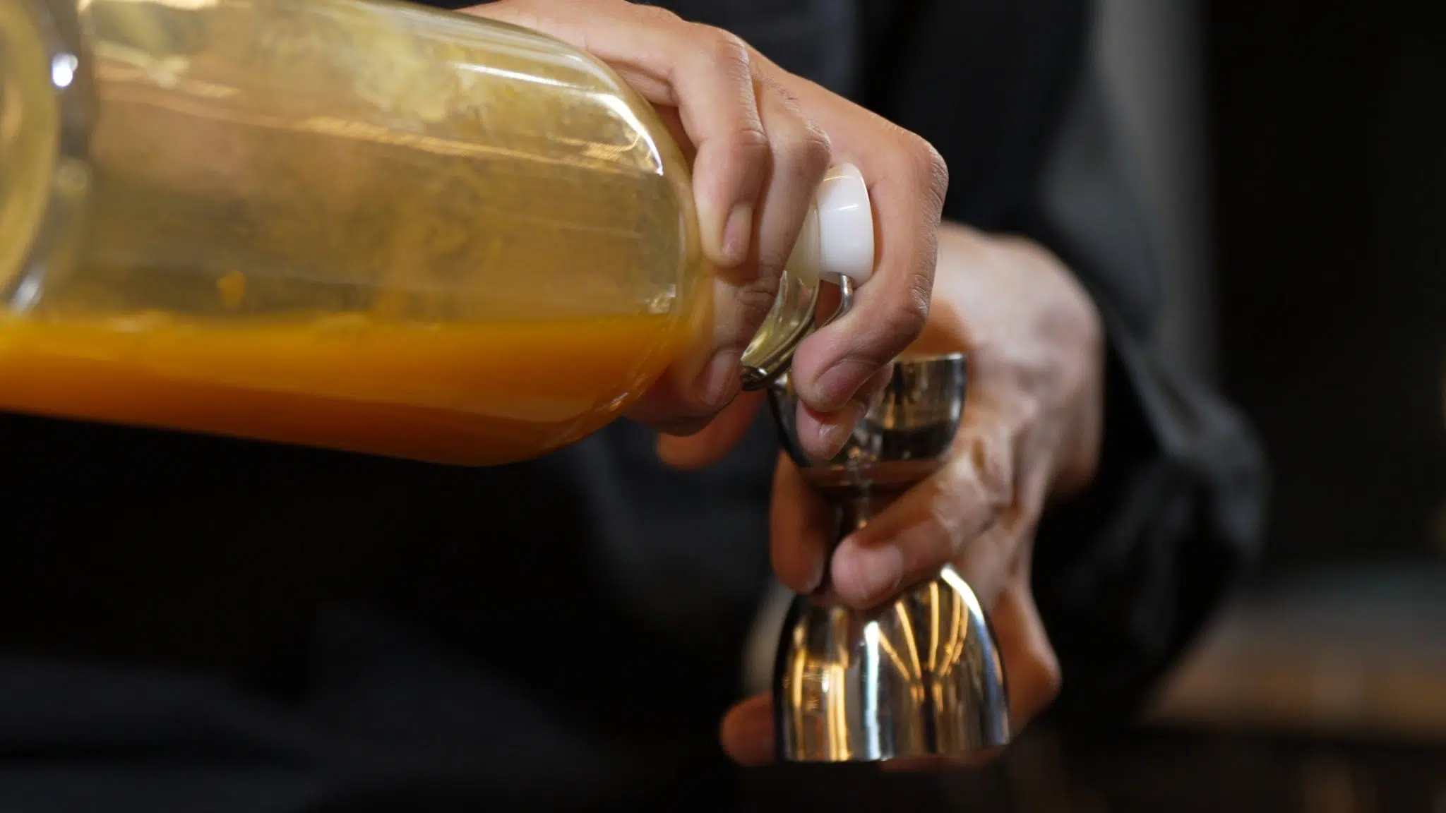 A shot of a bartender holding a bell jigger and pouring a liquid in it.