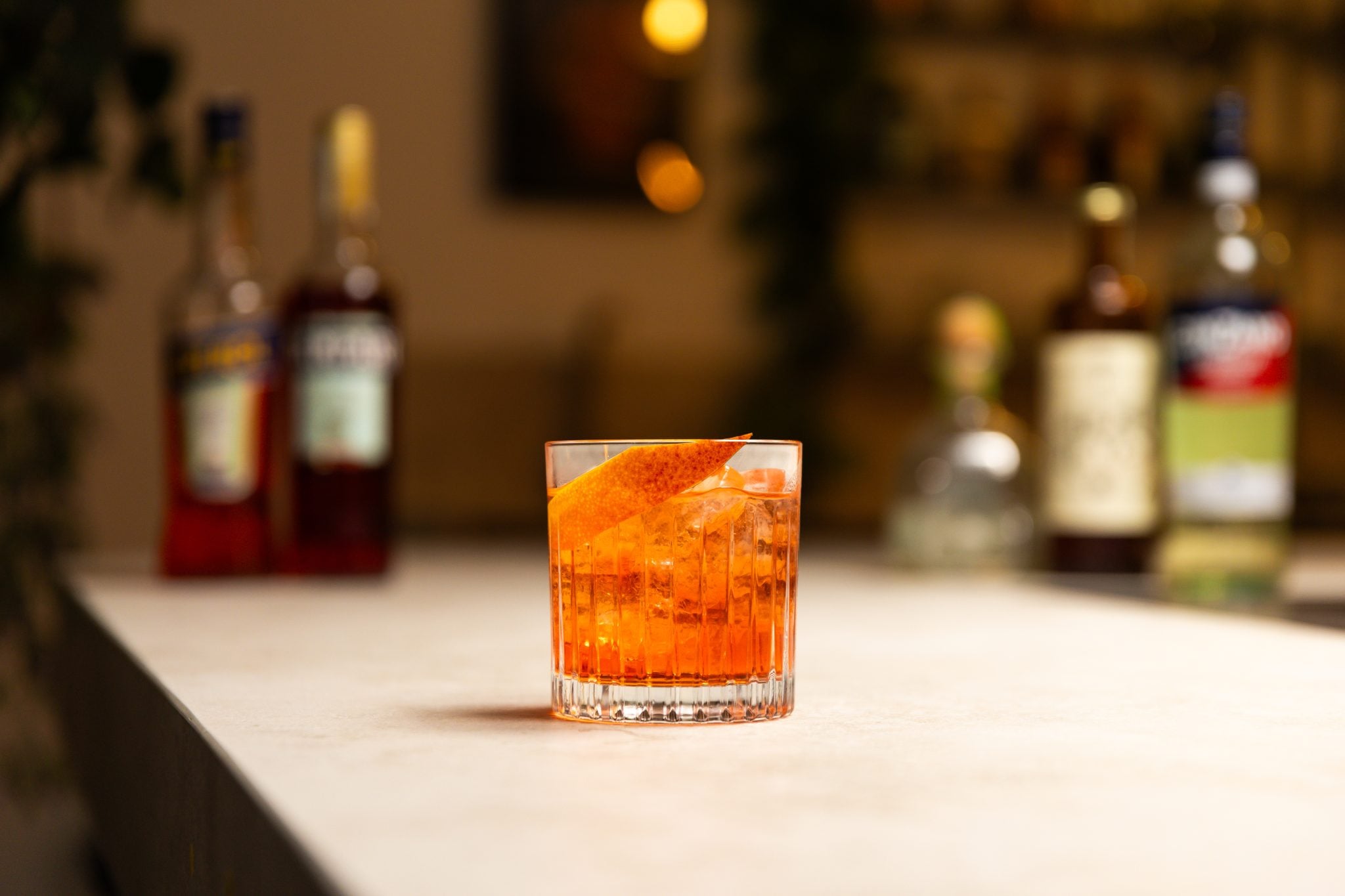 Blanco tequila, Campari, Aperol, vermouth bianco, and Ancho Reyes Ancho Chile Liqueur laid out on a white bar table
