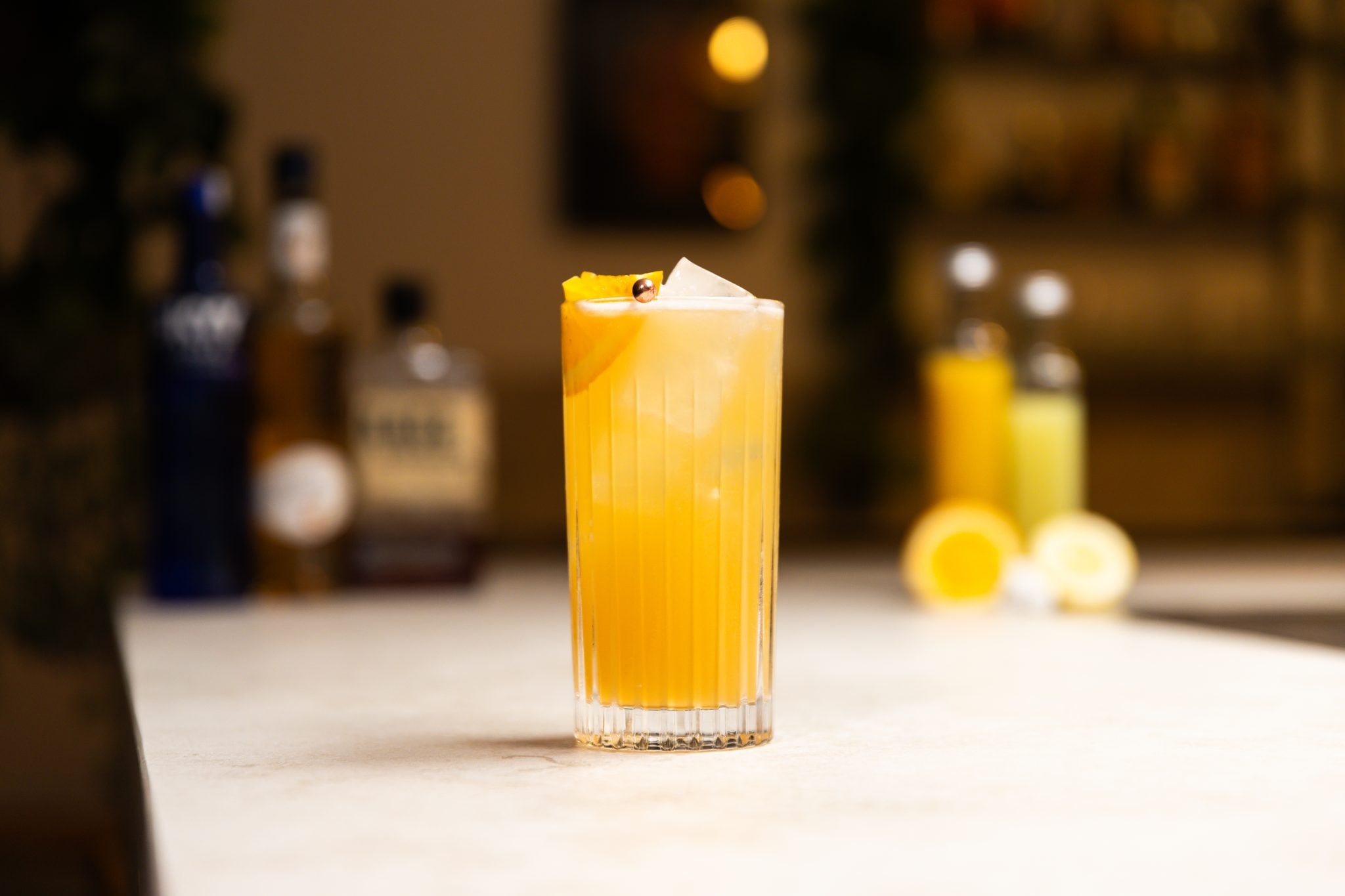 Bourbon, Vodka, peach schnapps, orange juice, sour mix, sugar cubes, half orange and lemon wedge laid out on a white bar table
