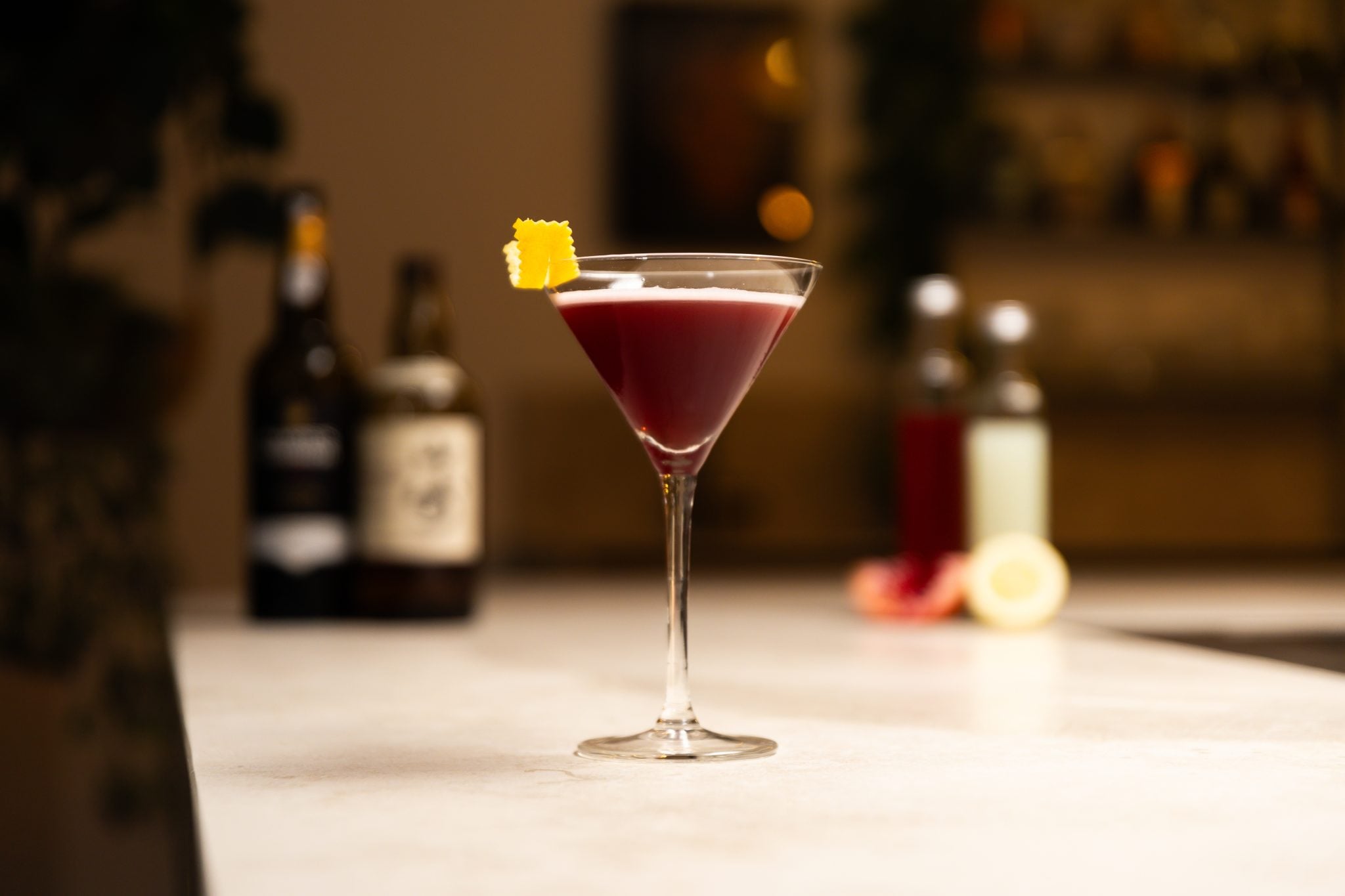 Japanese Whisky, pomegranate juice, Red Port wine, lemon juice, pomegranate and lemon laid out on a white bar table