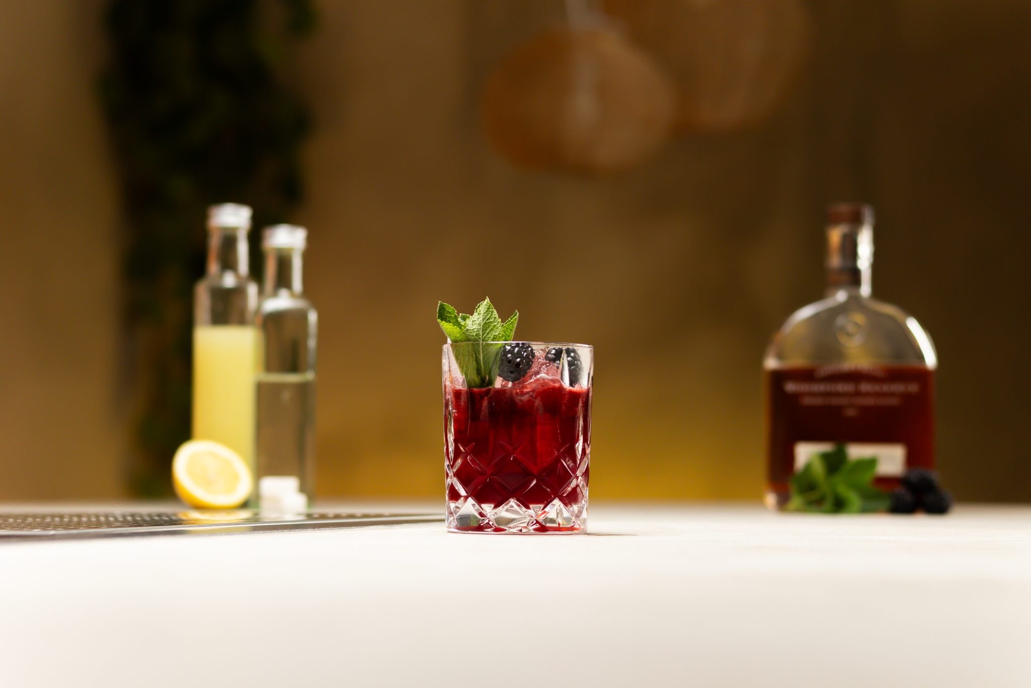 Bourbon, lemon juice, simple syrup, sugar cubes, lime and fresh mint sprig laid out on a white bar table