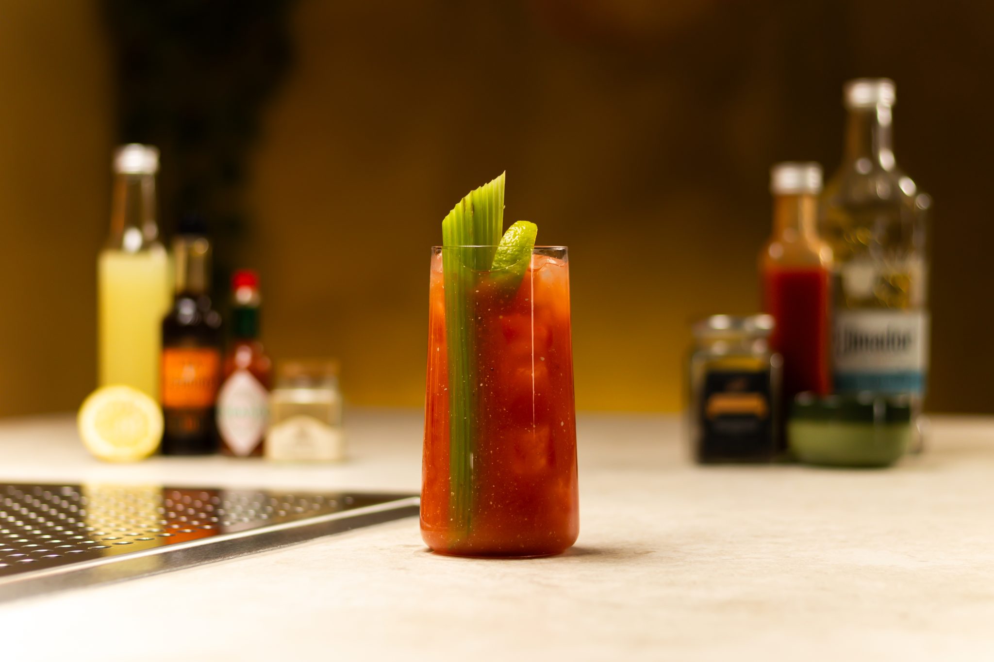 Tequila, tomato juice, lemon juice, Horseradish sauce, Worcestershire sauce, hot sauce, celery salt, and half lemon laid out on a white bar table