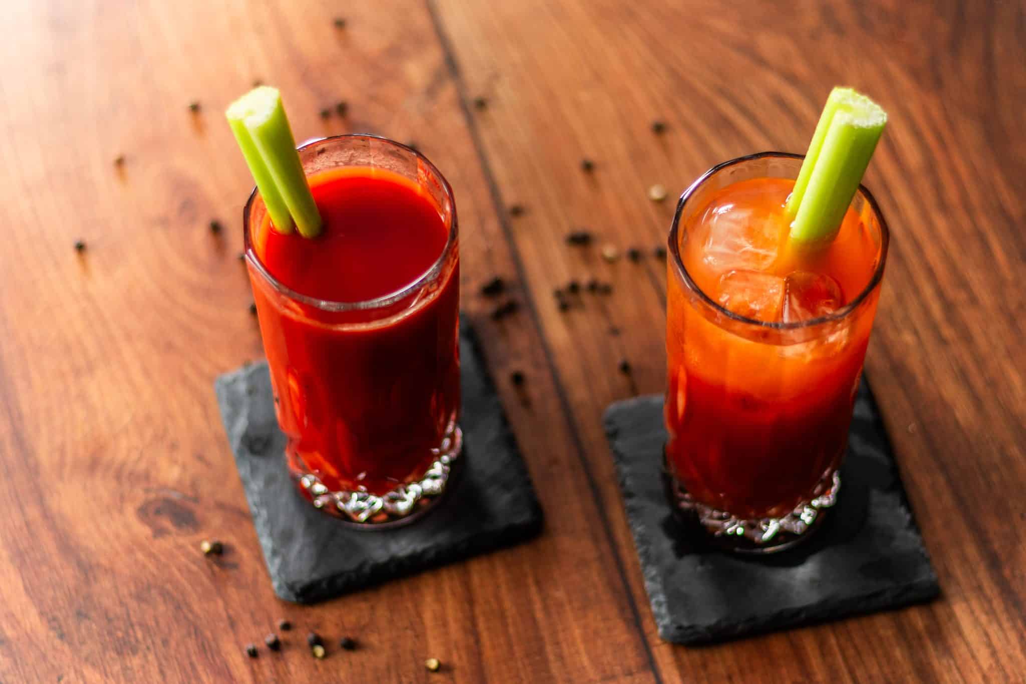 Two Bloody Mary cocktails, shot from above, in highball glasses on black stone coasters placed on a dark wooden table.