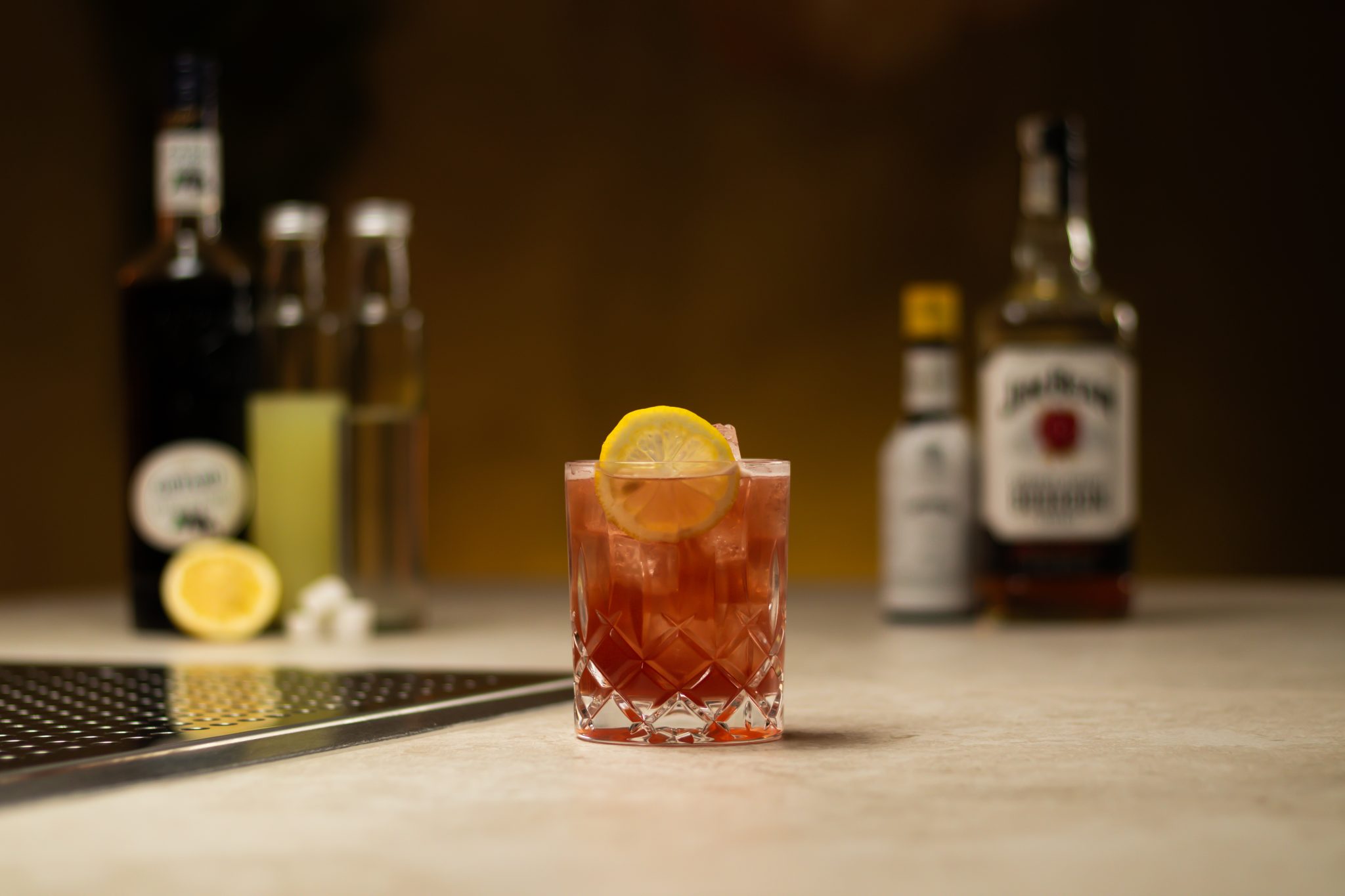 Bourbon, lemon juice, Creme de Cassis, Rich Syrup, Angostura aromatic bitters, sugar cubes and lemon laid out on a white bar table