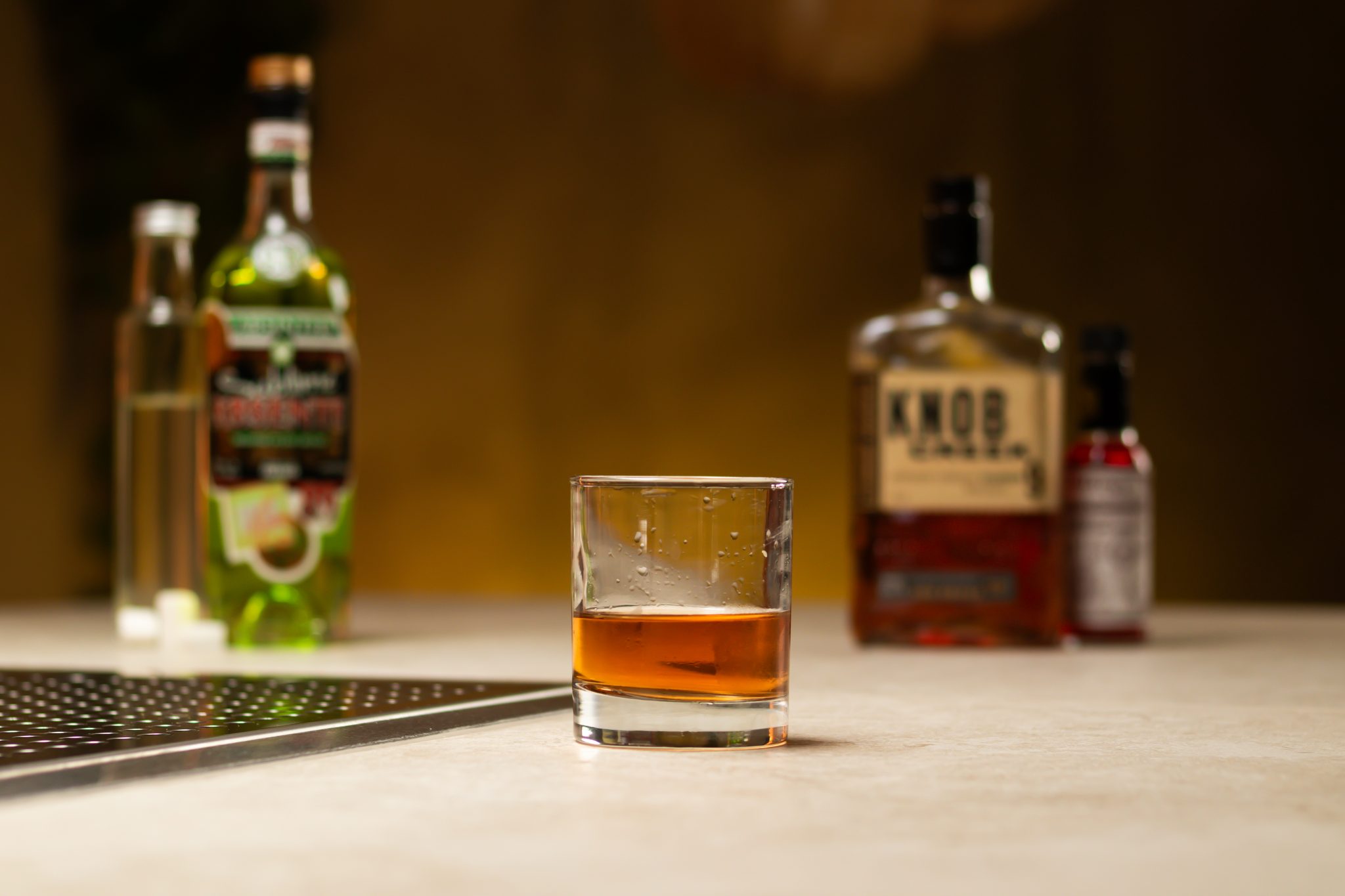 Bourbon, rich sugar syrup, Peychaud's Bitters, Absinthe and sugar cubes laid out on a white bar table