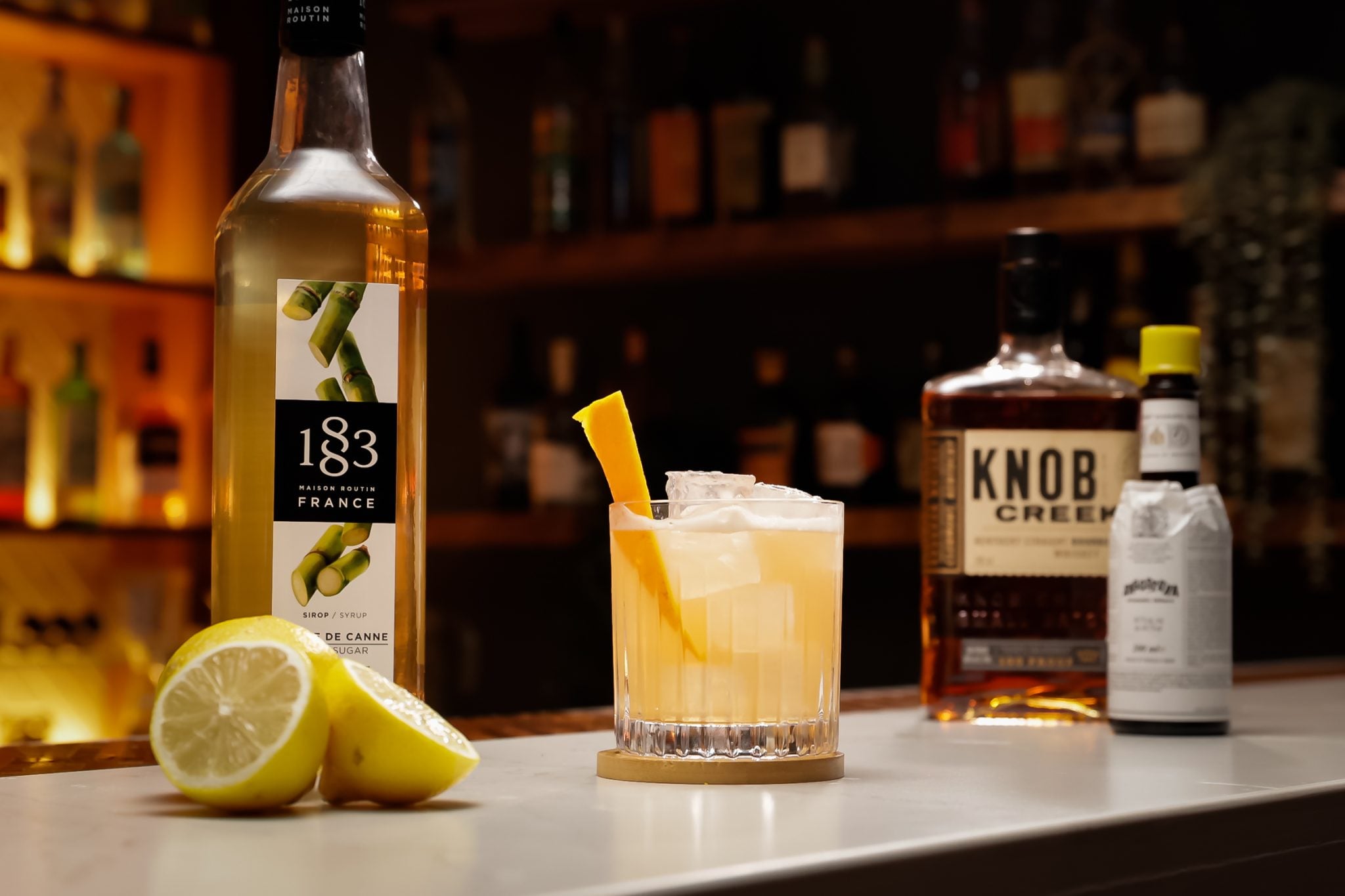 Whiskey, Simple Syrup and Angostura Bitters laid out on a white bar table