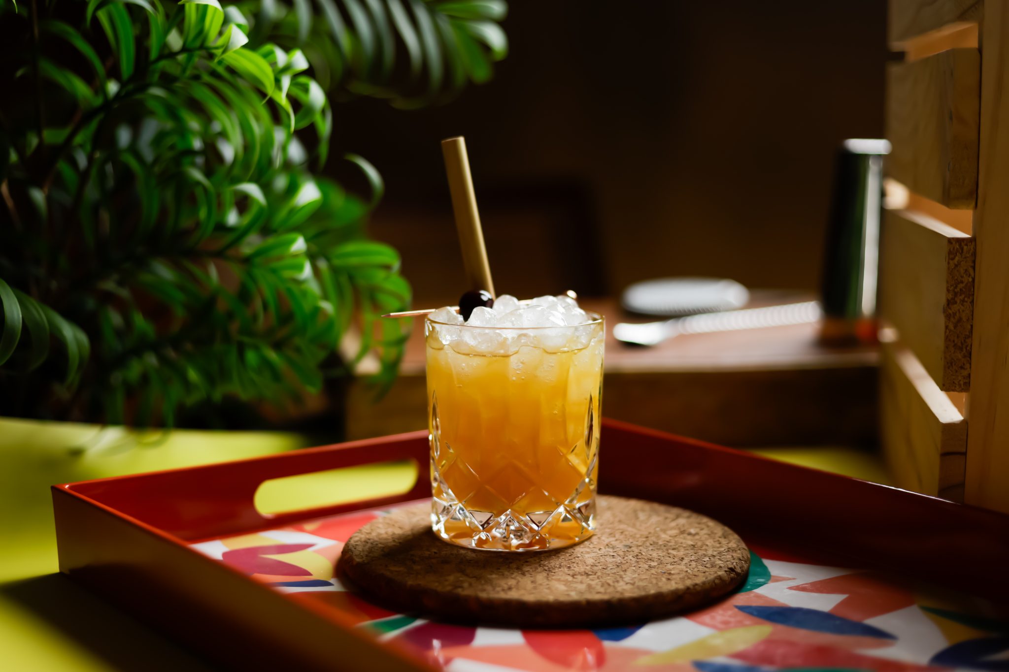 A side shot of a Brandy Cobbler cocktail in an old fashioned glass on a cork coaster placed on multicolor tray