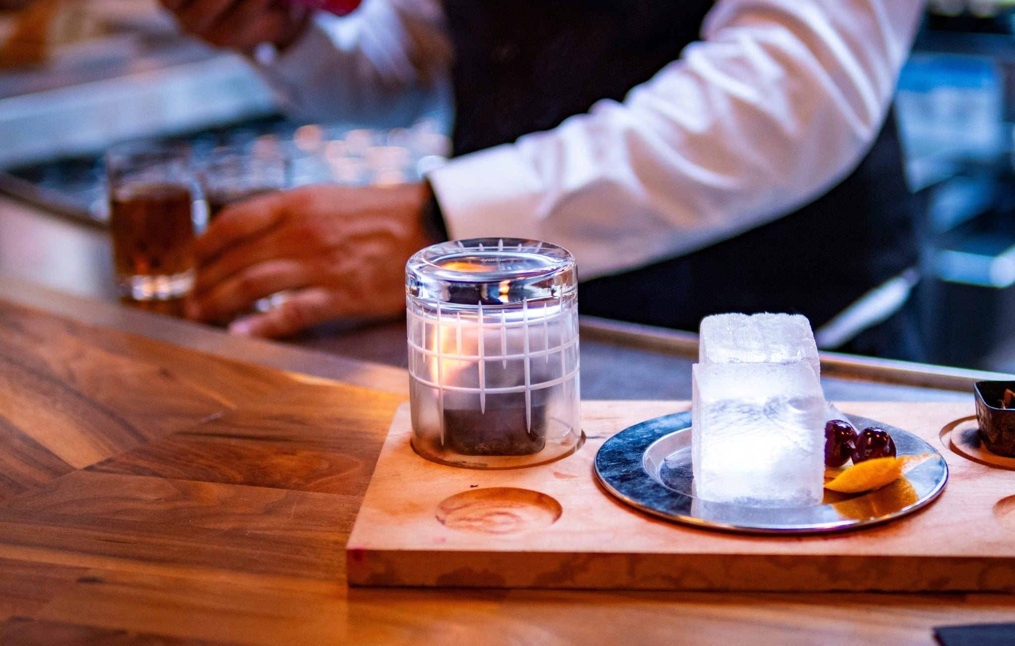 Shot of a low ball glass upside down on a wooden board, with a burning wood plank inside, preparing the glass for a Smoked Old Fashioned cocktail