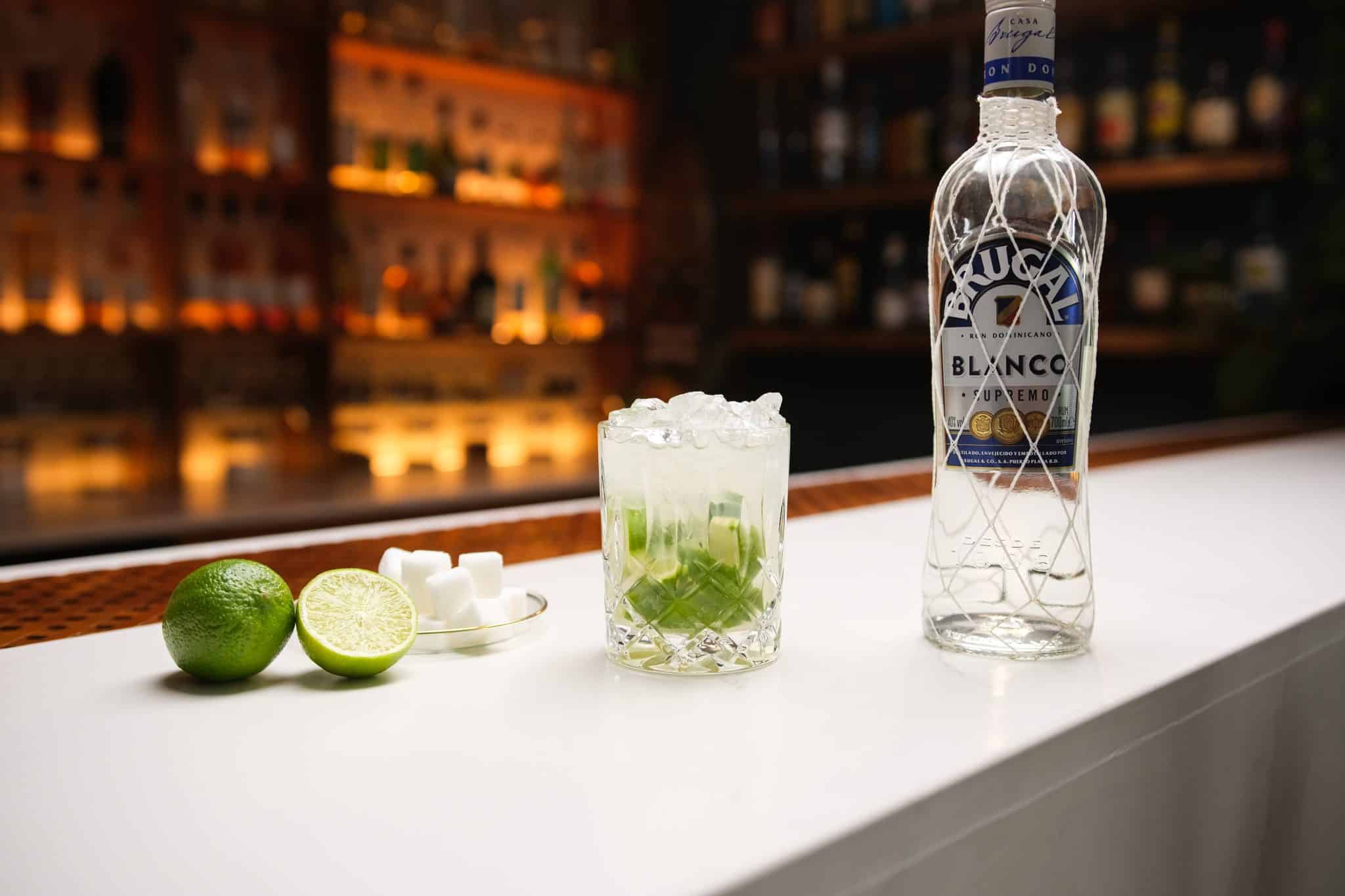 White rum, limes and sugar laid out on a white bar table.