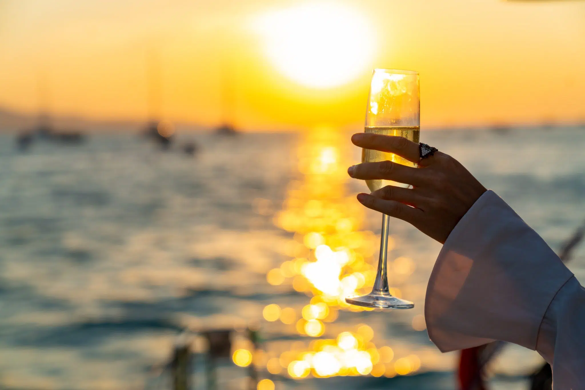 A shot of a hand holding a champagne flute by the bowl in front of a sunset view