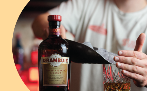 A shot of a bartender filling a Old Fashioned glass with ice with a Drambuie bottle on the side
