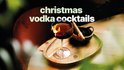 A cristmas vodka cocktail in a cocktail glass on a wooden board and a wooden table with a brown bowl with a cigar on the side