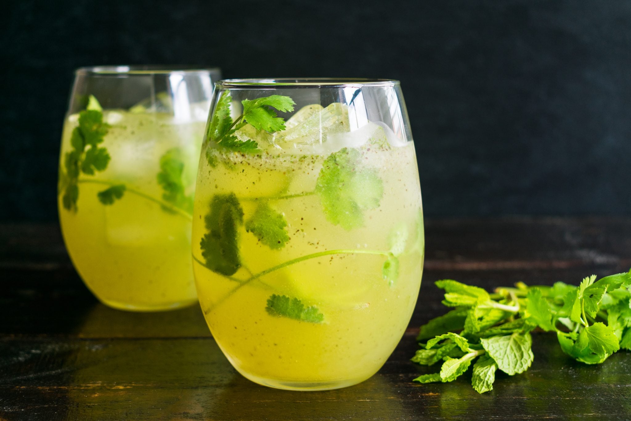 A shot of two cocktails in low ball glasses garnished with cilantro