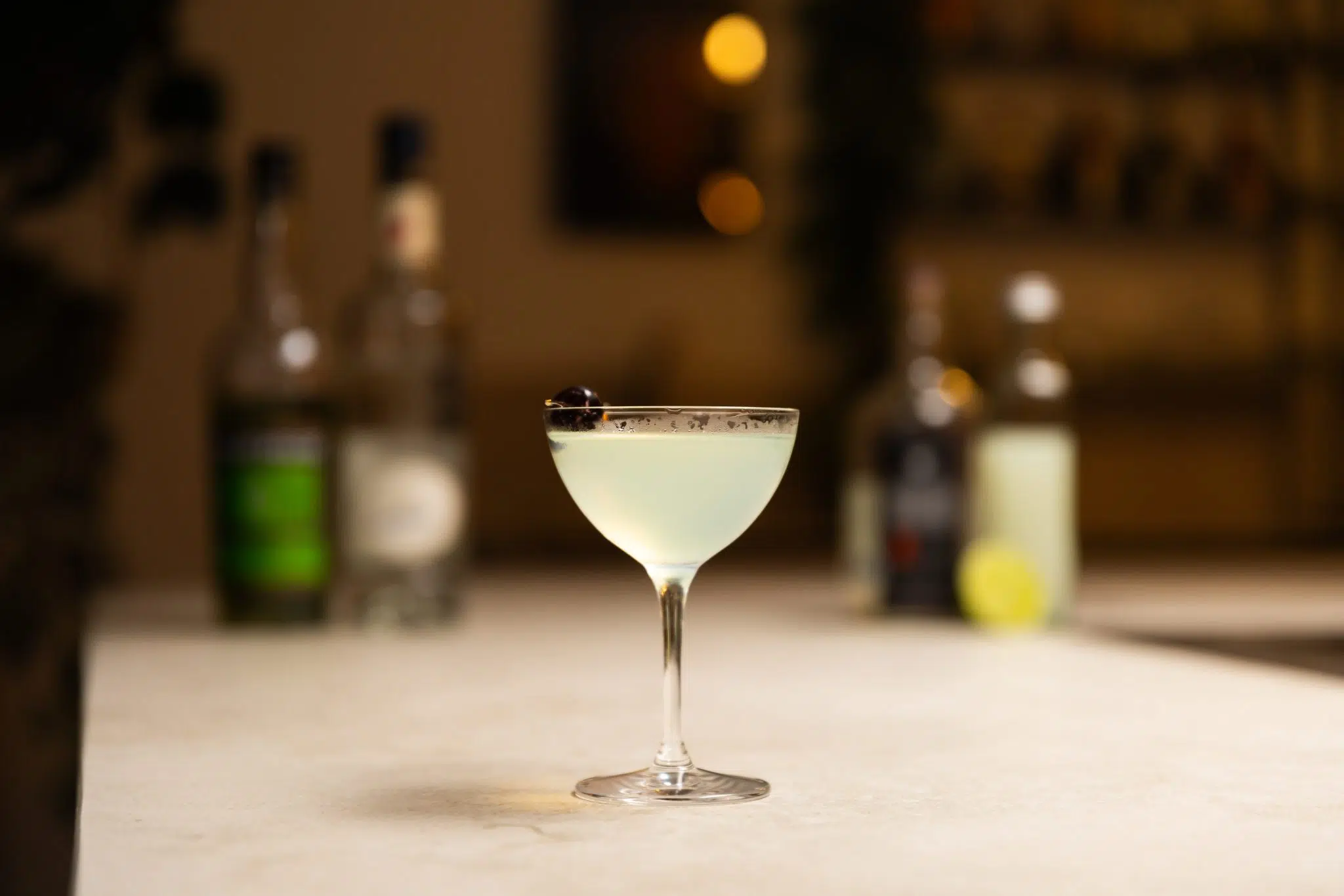 Mezcal, green chartreuse, maraschino liqueur, lime juice and lime laid out on a white bar table.