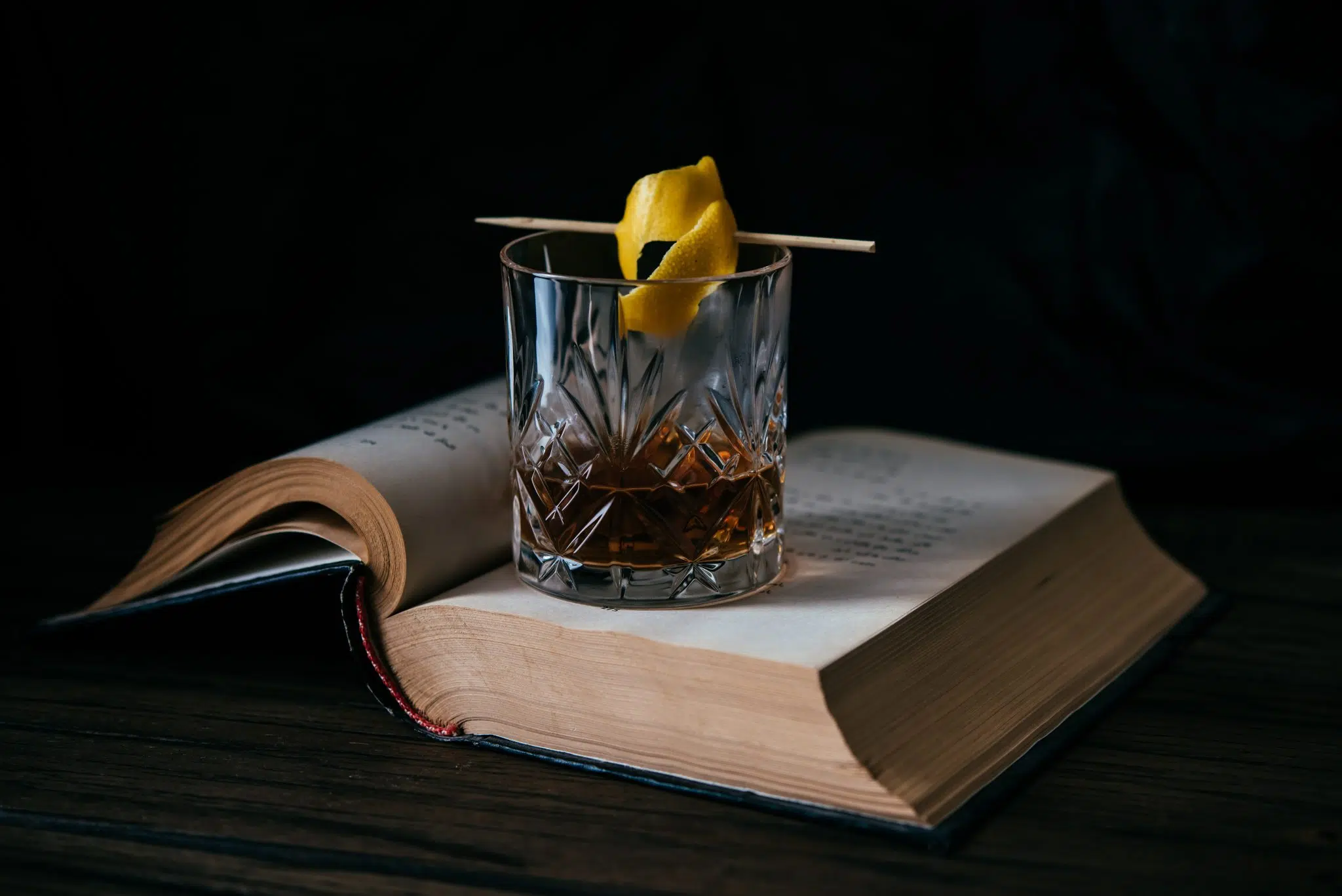 A shot of a cocktail in an Old Fashioned glass placed on a open book on a black background