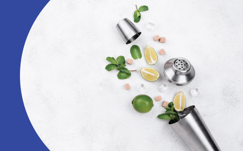 Cocktail shaker laying down open on a white surface and coming out a lime, three lime wedges, some mint sprigs, four ice cubes and seven brown sugar cubes