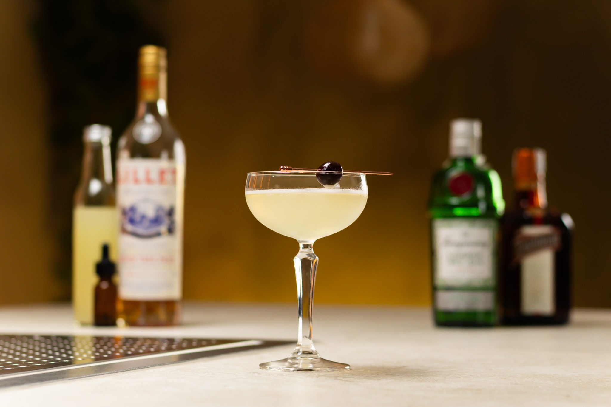 Gin, lemon juice, Lillet Blanc, Cointreau and Absinthe laid out on a white bar table