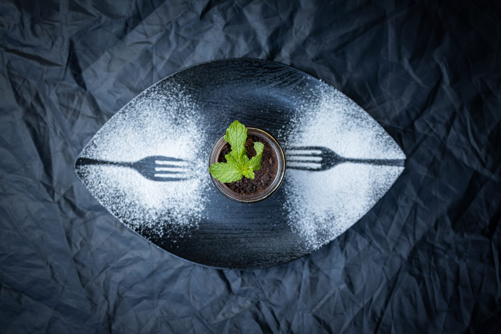 A shot from above of a cocktail dusted with a white powder making two fork patterns on the plate