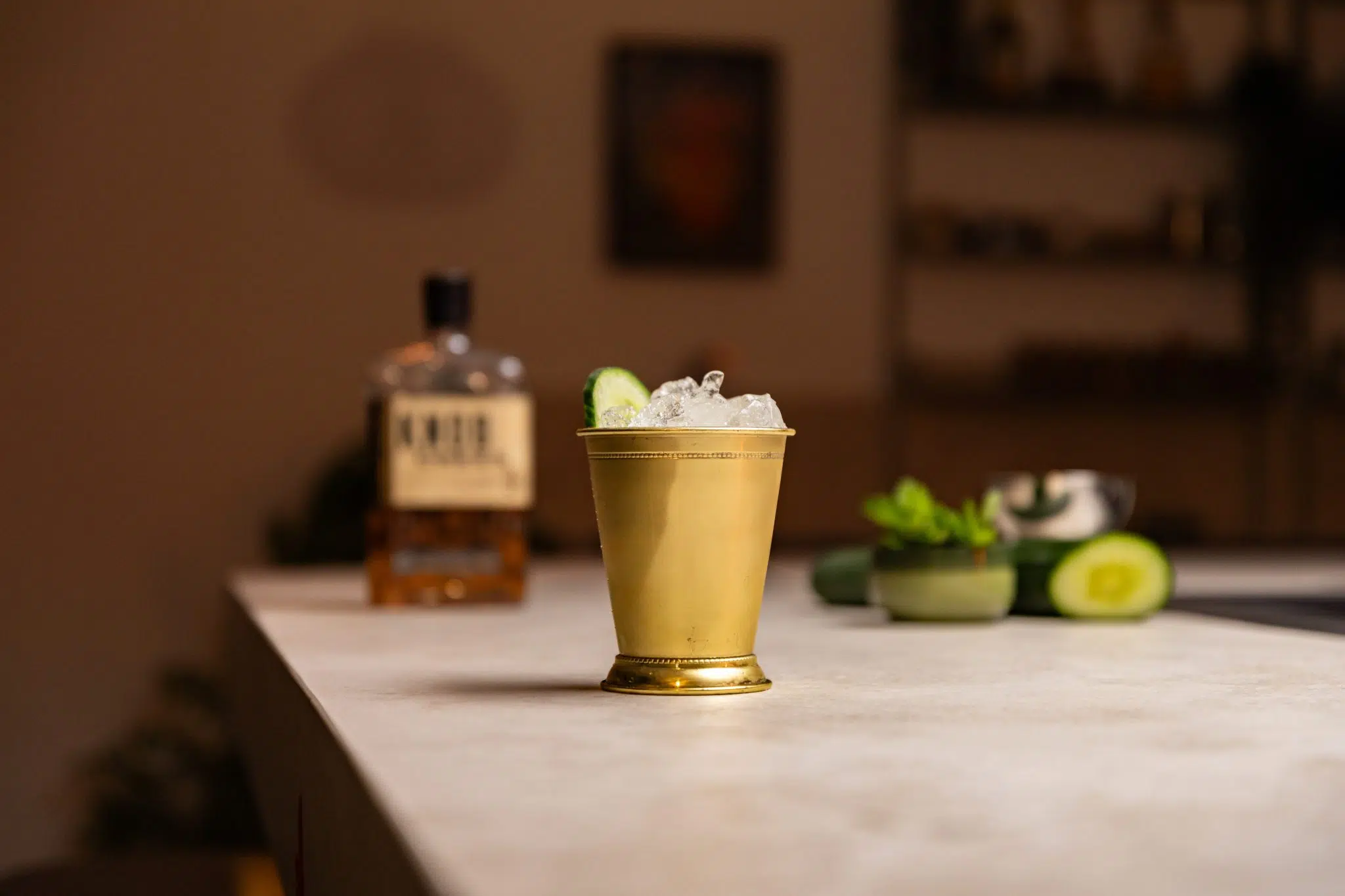 Bourbon, cucumber, honey, and mint leaves laid out on a white bar table