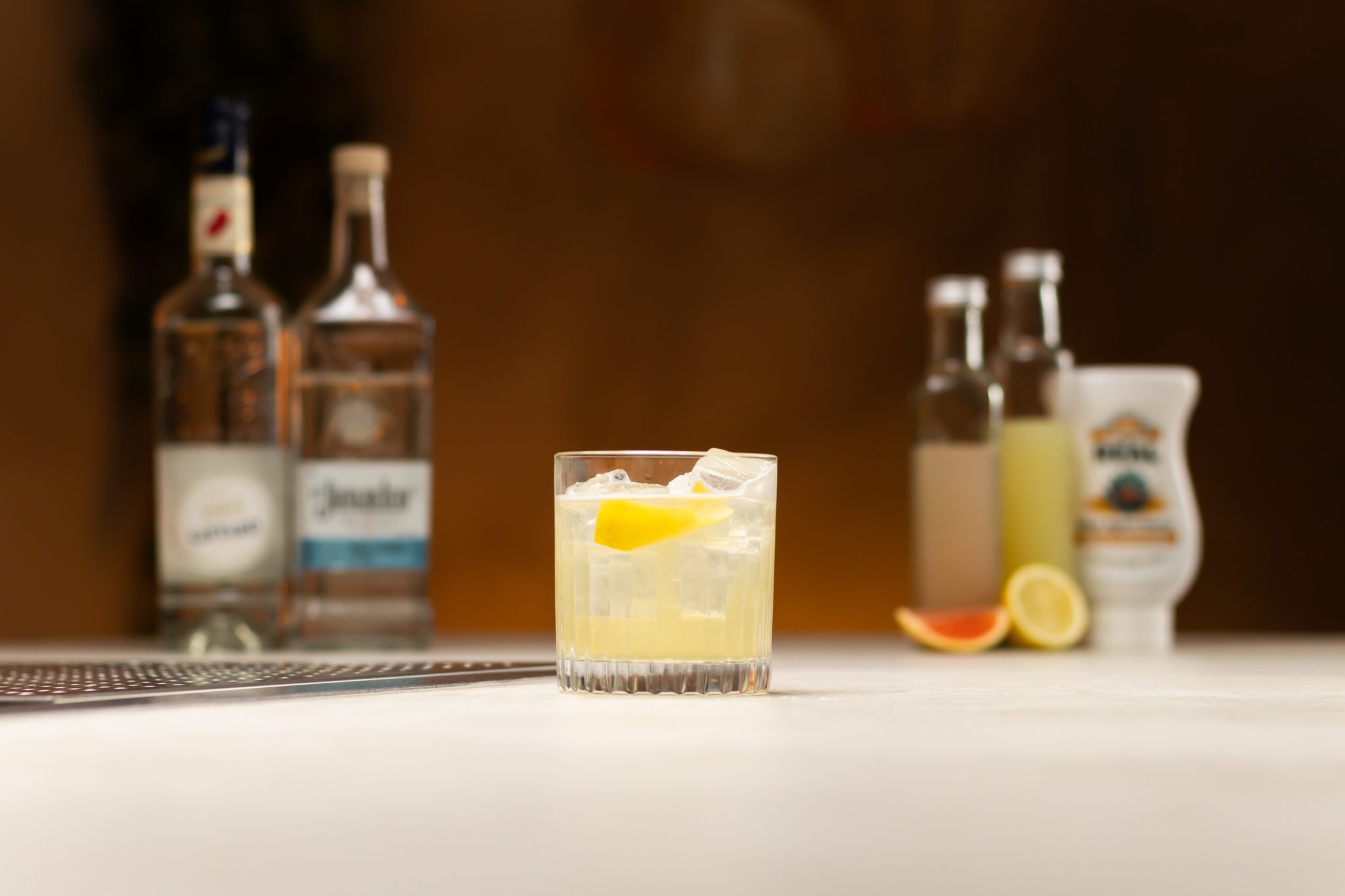 Maraschino liqueur, agave syrup, lemon juice, grapefruit juice, tequila, lime and grapefruit laid out on a white bar table