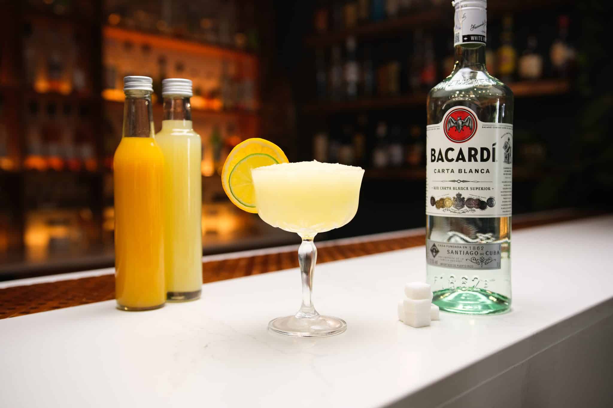 White rum, orange juice and lime juice laid out on a white bar table.