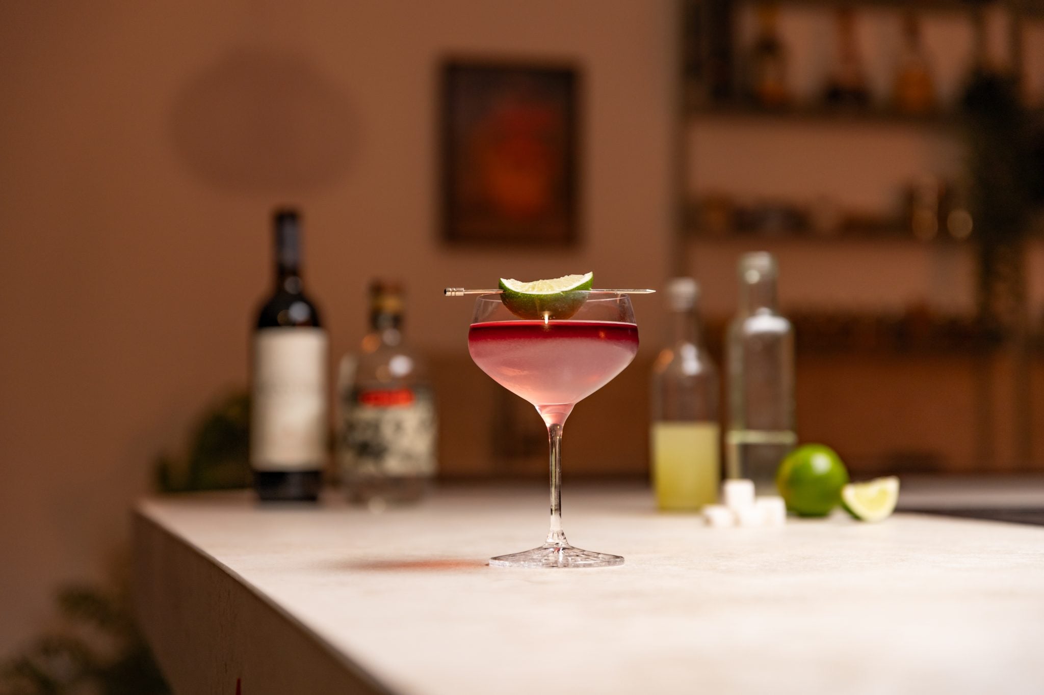 Tequila, red wine, lime juice, lime, simple syrup and sugar cubes laid out on a white bar table