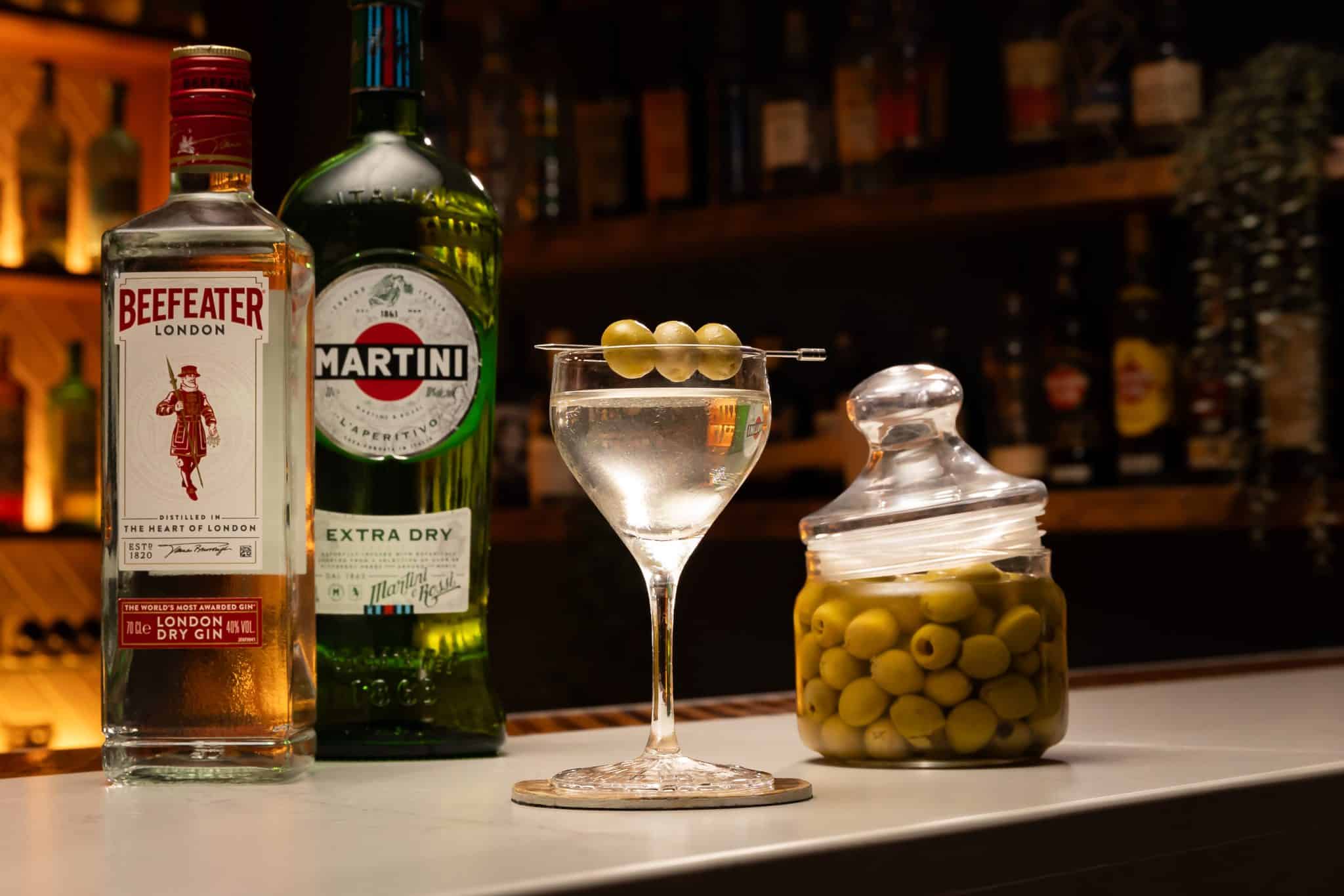 Gin, dry vermouth and olive brine laid out on a white bar table