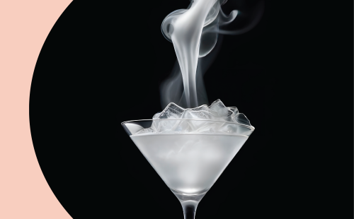 A martini glass filled with a transparent liquid and ice, smoking white smoke in front of a black background