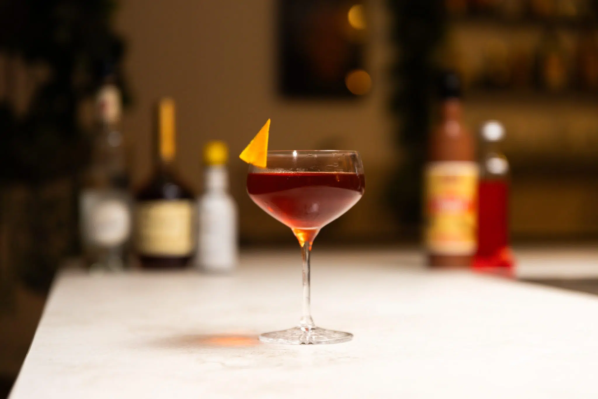 Cognac, red curaçao liqueur, raspberry syrup, maraschino liqueur, and Angostura aromatic bitters laid out on a white bar table