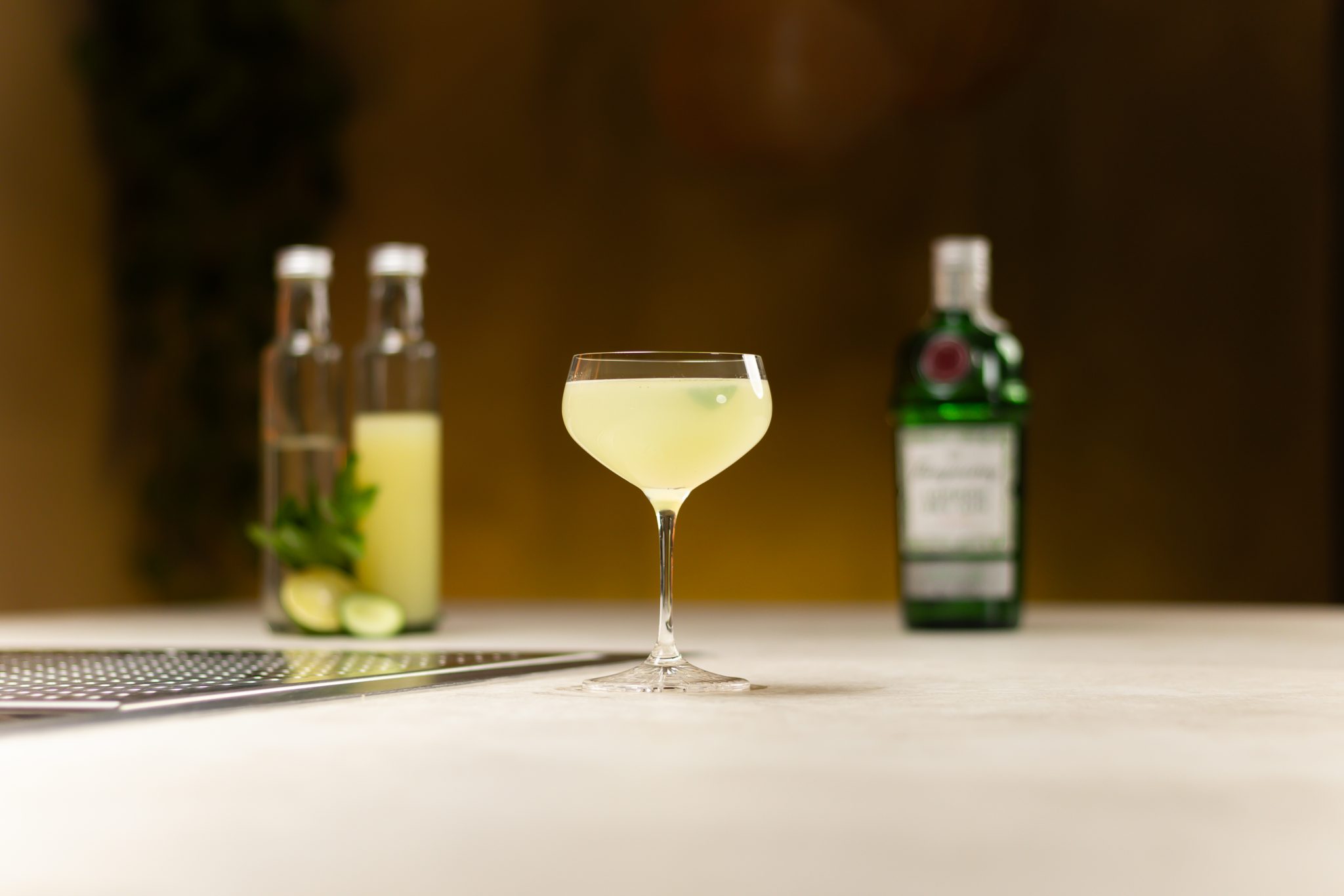 Gin, lime juice, simple syrup, mint leaves and cucumber laid out on a white bar table