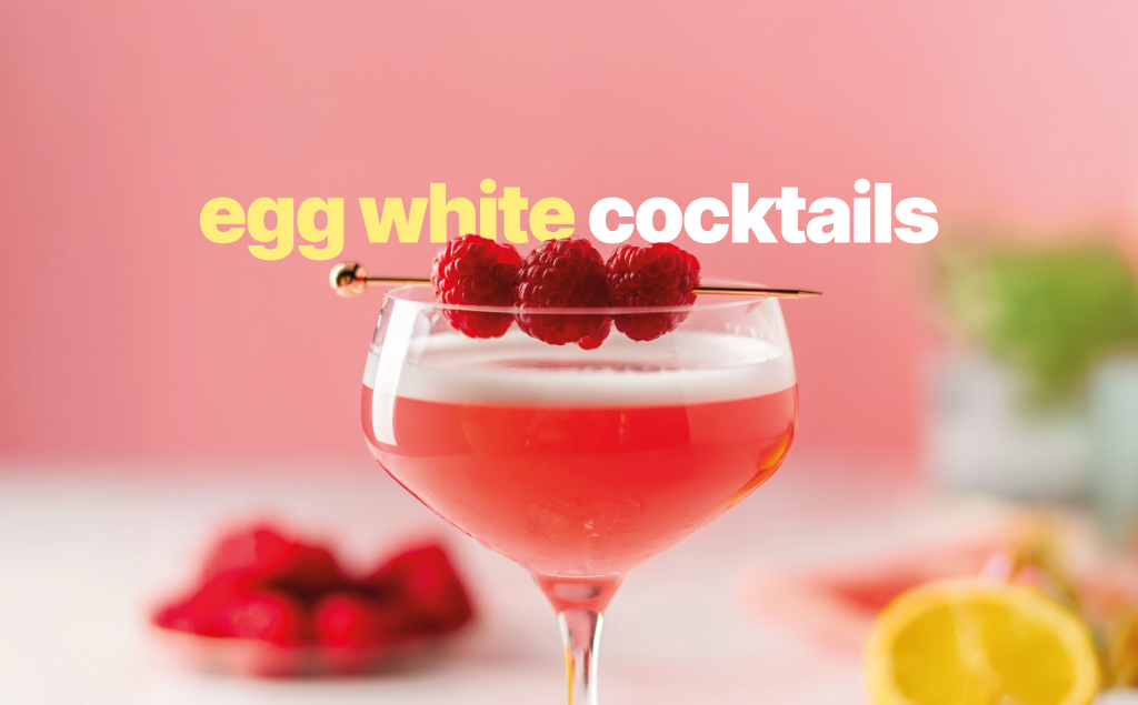 A egg white cocktail in a coupe glass garnished with three raspberries