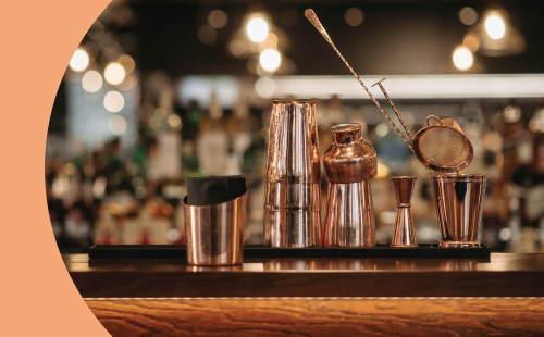 A shot of different bartender tools like cocktail shakers, jigger, bar spoons, etc, on a bar table in a restaurant or club