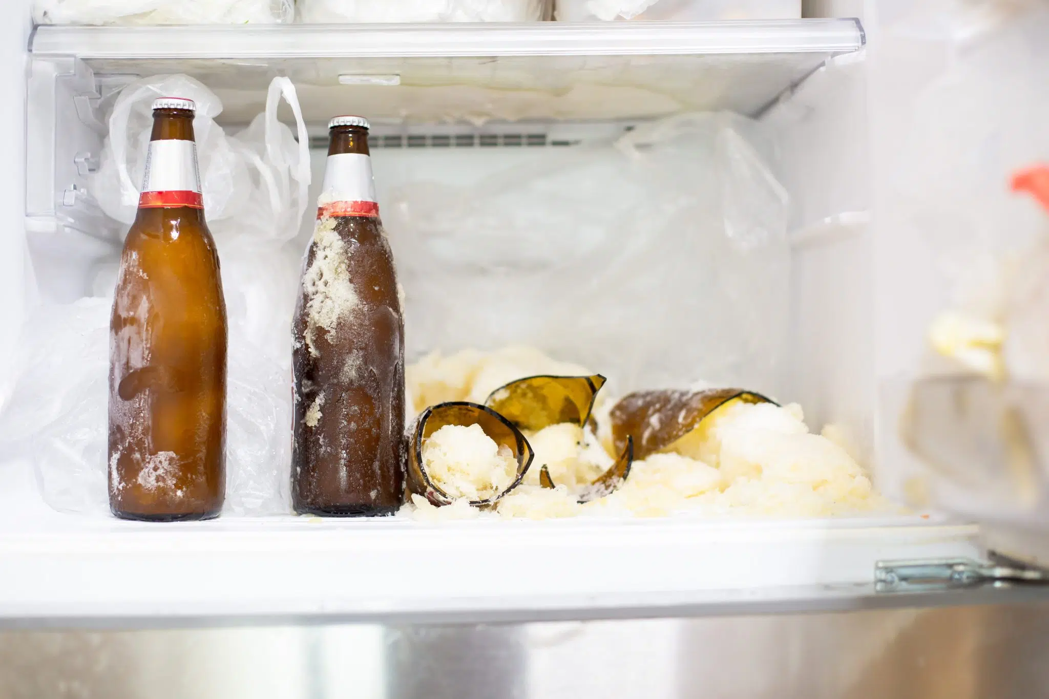 A shot of two cold beer bottles and two exploded beer bottles in a freezer 