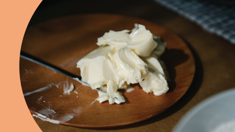 A shot of butter on a wooden plate with a knife on the side