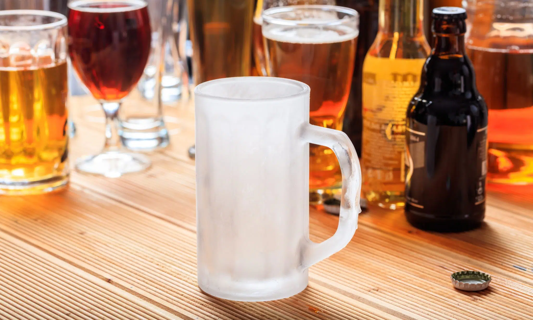 A side shot of a frozen beer glass on a table with a lot of different types of beer behind