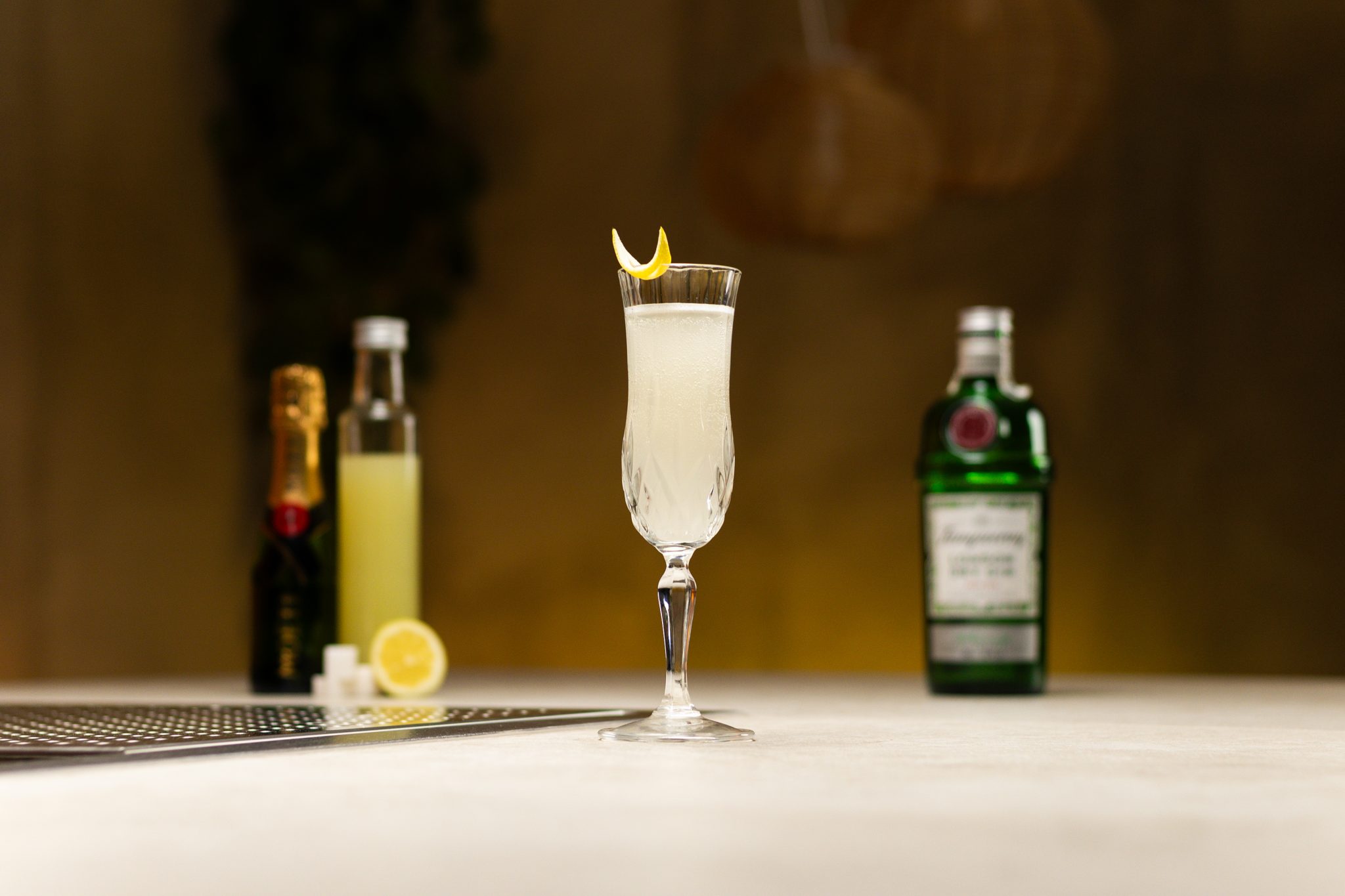 Gin, lemon juice, powdered sugar, lemons and champagne laid out on a white bar table