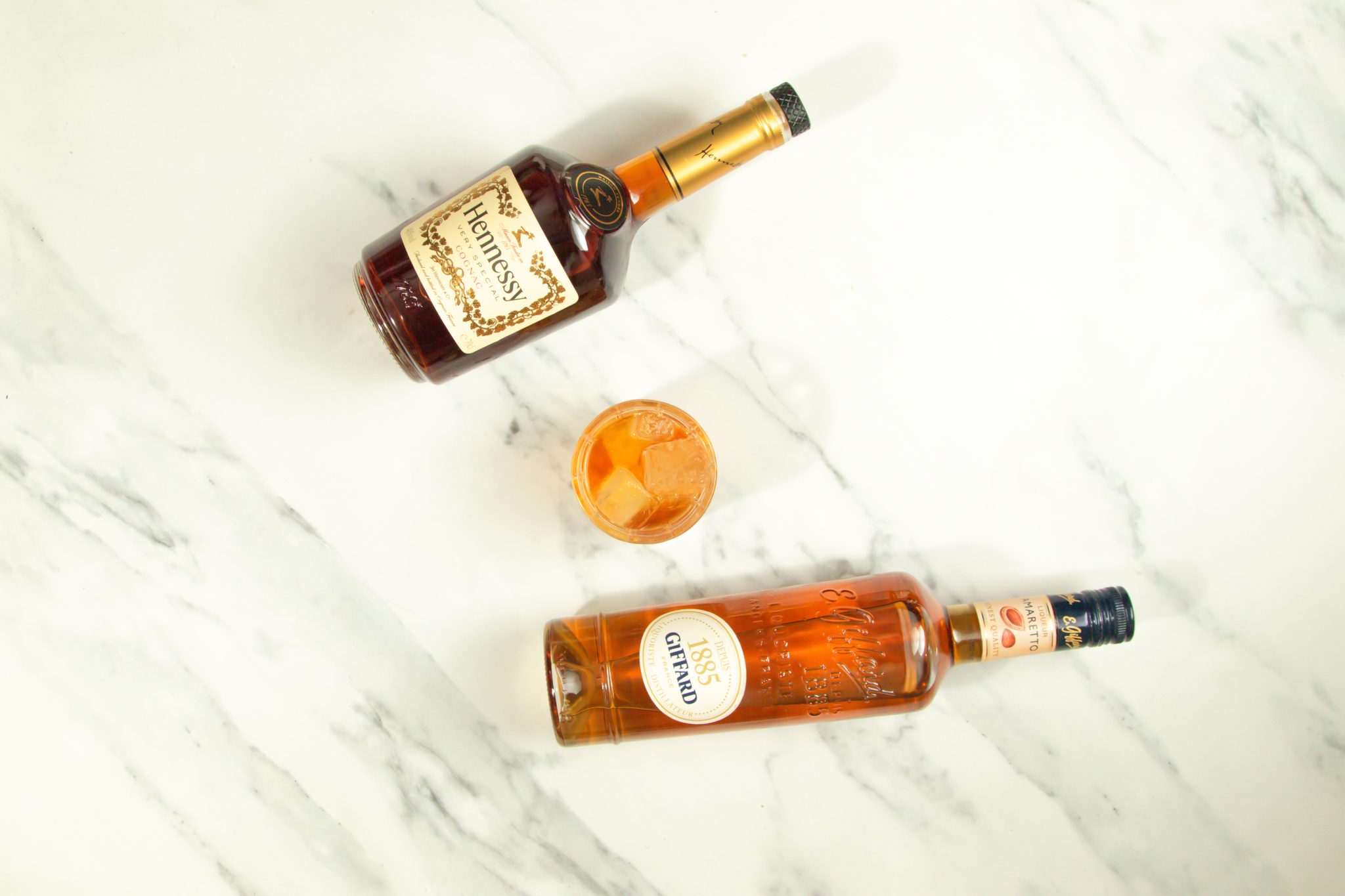 A French Connection cocktail, shot from above, in an Old Fashioned glass on a white marmol table with a Hennessy Cognac bottle and an Amaretto bottle around.