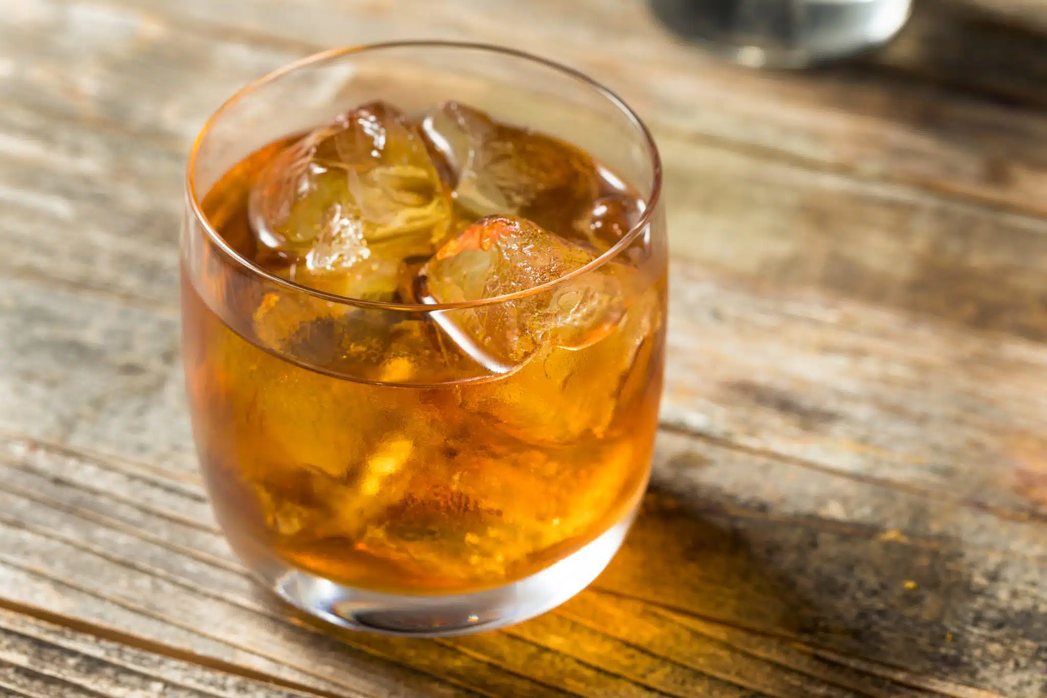 A glass of a French Connection cocktail with ice on a wooden surface.